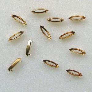 May include: A collection of 12 gold-toned metal settings for rhinestones or other embellishments. The settings are oval-shaped and have a flat back.