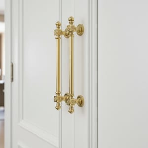May include: Close-up of a white door with two ornate, gold-colored door pulls. The pulls are vertical, with decorative detailing at the top, middle, and bottom. The door has a recessed panel design.