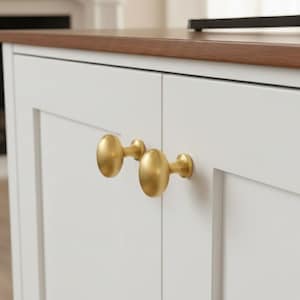 Op de afbeelding: Close-up van een witte kast met twee gouden ovale deurknoppen. De kast heeft een donkerbruin houten blad. De achtergrond is wazig en toont een open haard en een televisie.