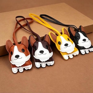 May include: Four corgi-shaped keychains in brown, white, yellow, and black. Each keychain has a leather strap and a smiling corgi face with brown ears and a white chest. The keychains are made of leather and have a stitched design.