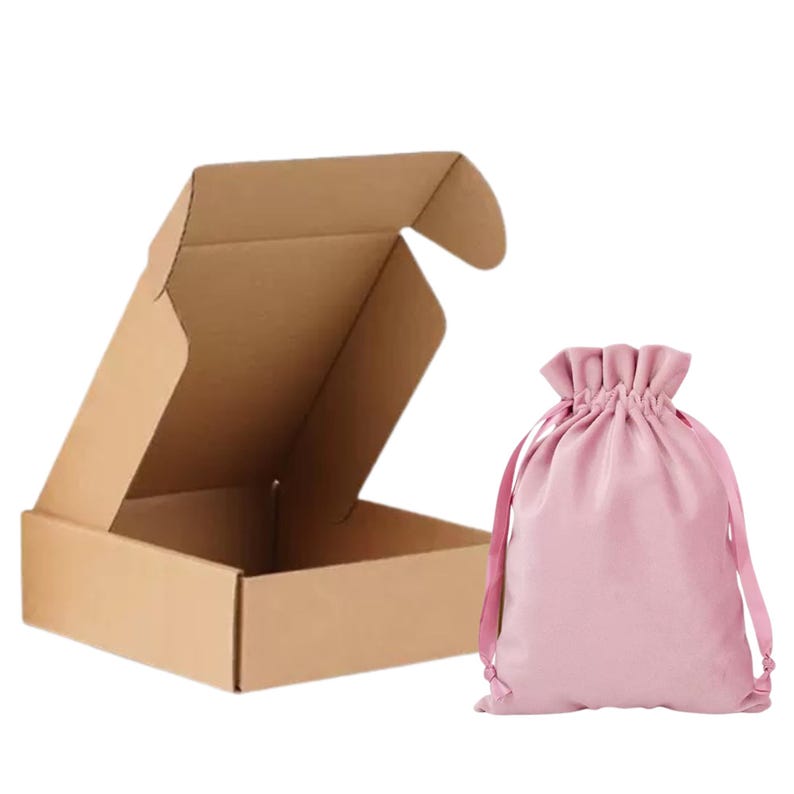 May include: An open, brown cardboard box next to a pink drawstring bag. The box is rectangular with flaps. The bag is gathered at the top with pink drawstrings. The background is white.