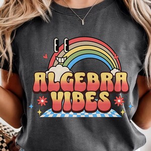 Peut inclure: T-shirt gris foncé avec un arc-en-ciel coloré et l'inscription "Algebra Vibes" dans une police rétro. Le t-shirt présente un motif de dessin animé avec des étoiles et un motif à carreaux en bas. Un tee-shirt décontracté et confortable.