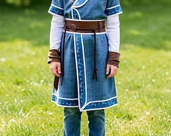 May include: A blue tunic with a white V-neck collar and white trim featuring a repeating pattern. The tunic is worn over a white long-sleeve shirt and blue jeans, and includes a brown belt with a circular buckle and brown wrist cuffs.