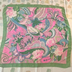 Peut inclure: Foulard carré en soie avec un motif floral et cachemire vibrant en rose, vert et bleu. Le foulard présente un motif central d'oiseau et une bordure verte. Le design général est complexe et coloré.