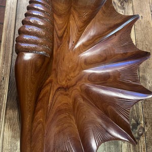 Peut inclure: Un grand bol en bois sculpté en forme de coquillage. Le bol est d'une riche couleur marron chaud avec un grain de bois visible. Le design présente une colonne texturée en spirale d'un côté et un bord festonné en forme d'éventail.