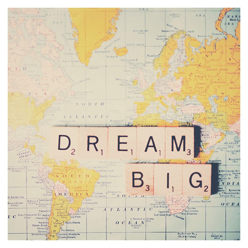 May include: A vintage world map with the words "DREAM BIG" spelled out in letter tiles. The tiles are arranged in two rows, with "DREAM" on top and "BIG" below. The map is faded and has a yellowed tint.