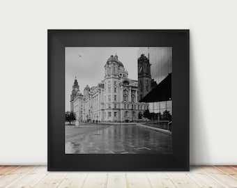 May include: A black and white photograph of a large building with a modern glass building reflected in the windows. The building is in a city setting and the ground is wet from rain.