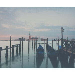 May include: A tranquil photograph of Venice, Italy, showing gondolas moored near a wooden pier. The image captures the calm water, the city's architecture, and a soft, muted colour palette, creating a sense of peace and serenity.