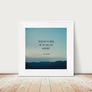 May include: A framed print with a white border. The artwork features a gradient blue sky over a mountain range. The quote "BLESSED ARE THE CURIOUS FOR THEY SHALL HAVE ADVENTURES" is displayed in white text. The author's name is below the quote.