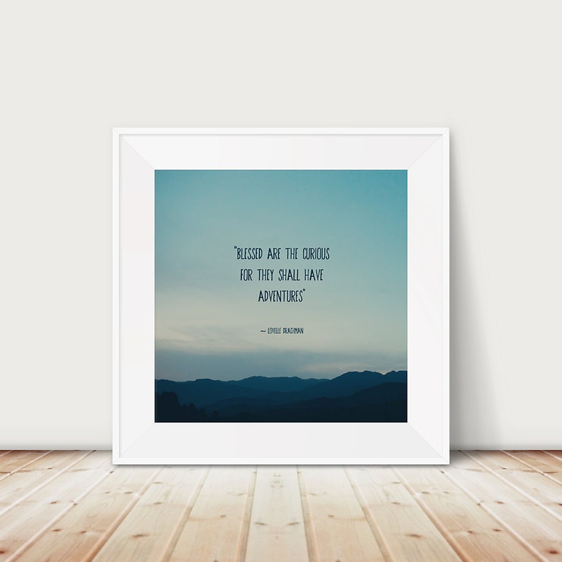 May include: A framed print with a white border. The artwork features a gradient blue sky over a mountain range. The quote "BLESSED ARE THE CURIOUS FOR THEY SHALL HAVE ADVENTURES" is displayed in white text. The author's name is below the quote.