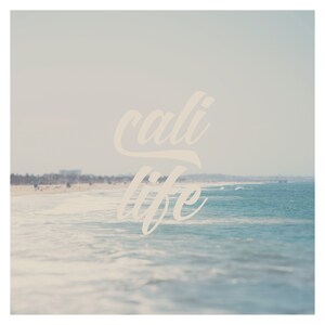 Puede incluir: Una serena escena de playa con las palabras "cali life" en una fuente cursiva superpuestas. El oc&eacute;ano es de color azul claro, con olas que ruedan suavemente hacia la orilla. El cielo tiene un tono suave y apagado, creando una atm&oacute;sfera tranquila.