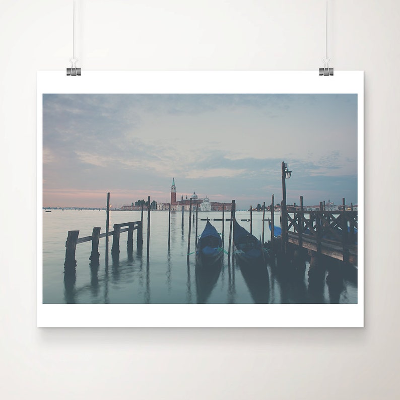 May include: A print depicting a Venetian scene with gondolas moored by a wooden pier. The image shows a tranquil waterscape with a church in the background under a pastel sky. The print is mounted on white paper.