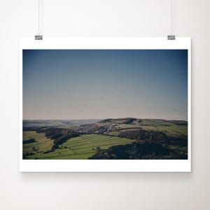 Puede incluir: Una vista panorámica de un paisaje verde ondulado con un pequeño pueblo en la distancia. El cielo es de un azul claro con algunas nubes blancas.