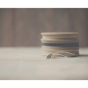 May include: A stack of wooden spools with cream-colored ribbon and black stripes. The ribbon is partially unraveled, revealing the striped pattern. The spools are stacked on a light-colored surface.
