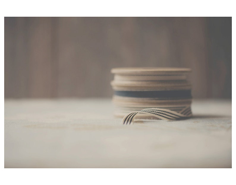 May include: A stack of wooden spools with cream-colored ribbon and black stripes. The ribbon is partially unraveled, revealing the striped pattern. The spools are stacked on a light-colored surface.