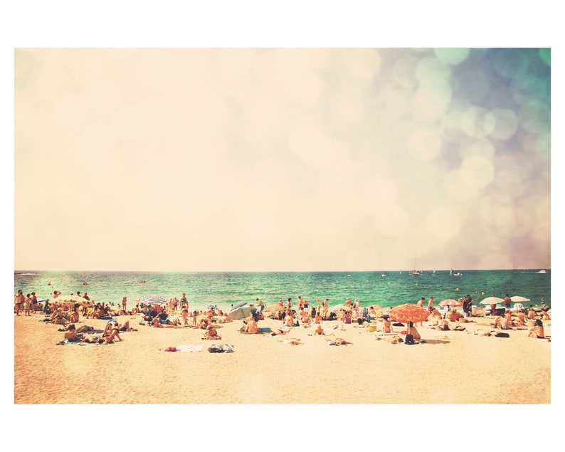 May include: A sunny beach scene with a large group of people enjoying the warm weather. The beach is sandy and the water is a bright turquoise blue. There are several umbrellas and beach chairs scattered throughout the scene.