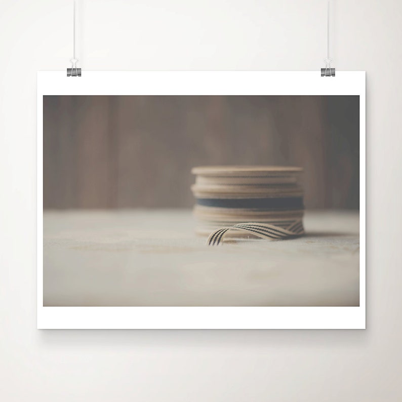 May include: A stack of wooden spools with a black and white striped ribbon. The spools are beige and brown, with a dark blue spool in the middle. The ribbon is partially unraveled, lying on a light-colored surface.