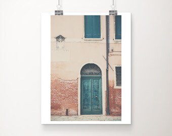 Könnte beinhalten: Gerahmter Druck einer Gebäudefassade mit türkisfarbener Tür und Fensterläden. Das Gebäude hat eine rosafarbene, beige Stuckfassade mit einem Ziegelsockel. Ein Metallrohr verläuft an der Seite.