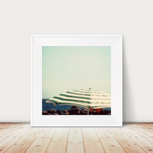 May include: A framed photograph of a green and white striped beach umbrella on a sandy beach with a blue sky in the background.