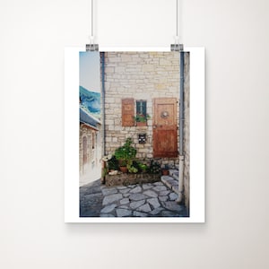 May include: A stone building with a wooden door and window, surrounded by potted plants. The building is located in a narrow alleyway with a stone path.