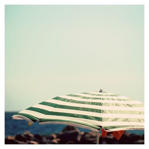 May include: A green and white striped beach umbrella with a wooden handle. The umbrella is open and is casting a shadow on the sand.