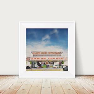 Könnte beinhalten: Ein Vintage-Foto eines Karnevals-Imbissstandes mit blauem Himmel und weißen Wolken im Hintergrund. Der Stand hat ein rot-weiß gestreiftes Vordach und ein Schild mit der Aufschrift "Caramel Apples Cotton Candy" und "Caramel Corn Candy Apples".