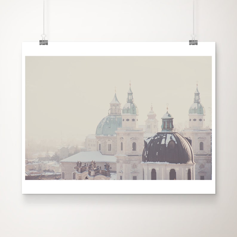 May include: A misty cityscape with several white and green domed churches. The buildings are covered in snow and the sky is a pale blue.