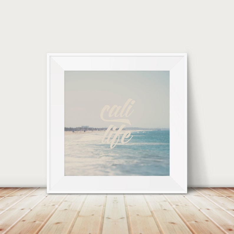 Puede incluir: Una impresi&oacute;n enmarcada que presenta una escena de playa con las palabras "cali life" en una fuente cursiva. La imagen muestra una playa arenosa, olas del oc&eacute;ano y un cielo azul claro. El marco es blanco.