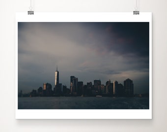 May include: A silhouette of the New York City skyline with the Freedom Tower in the center, against a dark cloudy sky.