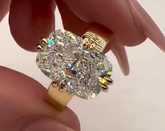 May include: A gold ring featuring a large, oval-shaped cluster of clear gemstones. The ring's band is a simple, polished gold, and the gemstones are set closely together, creating a sparkling, eye-catching effect. The ring is held up by a hand.