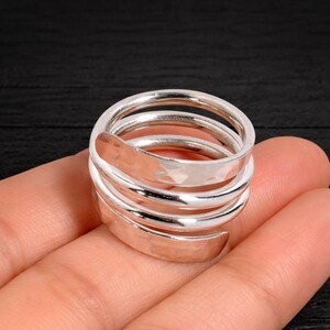 May include: A silver spiral ring with a hammered finish. The ring coils around the finger, forming multiple layers. The shiny metal ring has a contemporary design. The ring's diameter is approximately 2 cm.