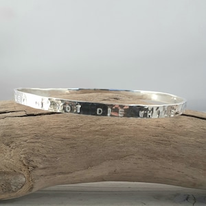May include: A silver bangle bracelet with the inscription "Let me not die while I'm still learning".