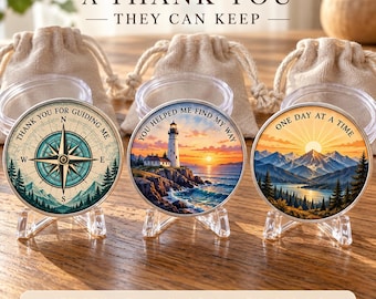 May include: A set of three round coins on clear stands, each with a unique graphic and text: a compass with 'THANK YOU FOR GUIDING ME', a lighthouse with 'YOU HELPED ME FIND MY WAY', and mountains with 'ONE DAY AT A TIME'.