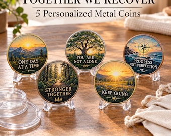 May include: Five round metal coins featuring colorful landscape illustrations and motivational text: ONE DAY AT A TIME, YOU ARE NOT ALONE, PROGRESS NOT PERFECTION, STRONGER TOGETHER, and KEEP GOING. Each coin is displayed on a clear plastic stand.