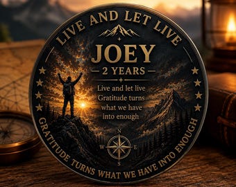 Op de afbeelding: Een ronde medaille met een berglandschap bij zonsondergang en het silhouet van een wandelaar. De tekst luidt: LIVE AND LET LIVE, JOEY, 2 YEARS en Gratitude turns what we have into enough. Onderaan staat een kompasroos met sterren aan de zijkanten.