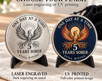 May include: Two round sobriety coins on black stands. The left coin is silver-toned metal with laser-engraved phoenix and text. The right coin features a full-color UV-printed phoenix on a dark blue background. Both read: ONE DAY AT A TIME, 5 YEARS SOBER, STILL RISING.