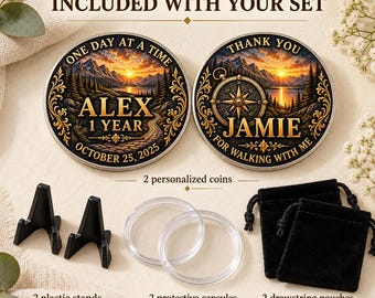 May include: Two round personalized coins featuring a sunset mountain landscape, one inscribed with ALEX 1 YEAR OCTOBER 25, 2025 and the other with JAMIE. Includes two black plastic display stands, two clear protective capsules, and two black drawstring pouches.