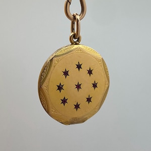 May include: A gold-colored, round pendant with a decorative border and eight star-shaped accents, each with a dark red center. The pendant is attached to a gold chain and clasp.