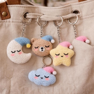 May include: Handmade crochet keyrings featuring a sleeping moon, bear, star, and cloud. Each charm has a sleeping cap in pastel colours, including blue, pink, and yellow. The keyrings are attached to silver rings.