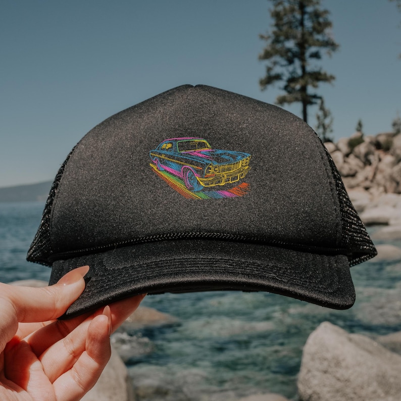 May include: Black trucker hat with a mesh back and a curved brim. The front of the hat features a colorful embroidered design of a classic car. The car is outlined in bright colors, including blue, yellow, and pink.