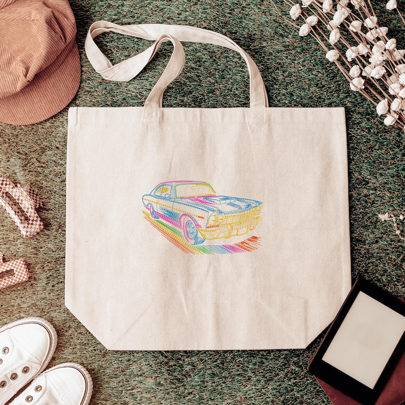 May include: A beige tote bag with a colorful embroidered image of a classic car. The car design features a rainbow of colors, including blue, yellow, and pink. The bag has two beige handles and is made of a sturdy fabric.