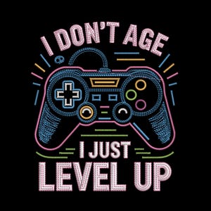 Puede incluir: Un diseño bordado sobre fondo negro que muestra un mando de videojuego con contornos en puntadas rosas, azules y amarillas. El texto I DON'T AGE I JUST LEVEL UP aparece en letras bordadas blancas, rosas y azules con líneas decorativas.