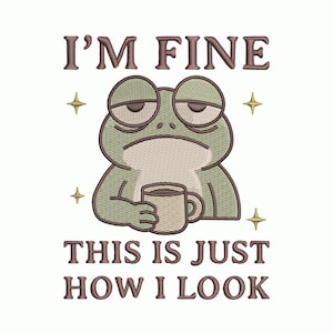 May include: An embroidered design featuring a cartoon frog with droopy eyes holding a coffee mug. The text above reads "I'M FINE", and below the frog, it says "THIS IS JUST HOW I LOOK". The frog is green, and the text is brown.