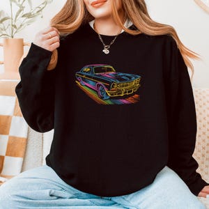 May include: Black sweatshirt featuring a colorful, neon-outlined illustration of a classic car. The car design includes details like the grille, headlights, and wheels, with a rainbow-colored trail beneath it. The sweatshirt is a solid black color.