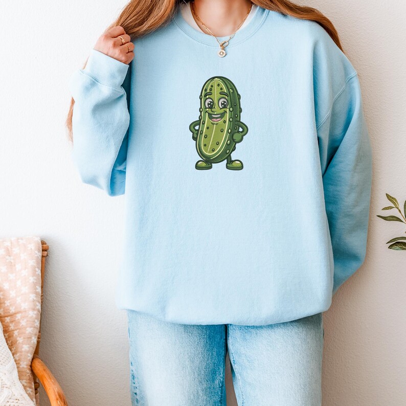 Może przedstawiać: Jasnoniebieska bluza z nadrukiem postaci z kresk&oacute;wki - og&oacute;rka. Zielony og&oacute;rek z ż&oacute;łtymi detalami uśmiecha się i ma ręce i nogi. Bluza wykonana jest z miękkiego materiału i ma wygodny kr&oacute;j.