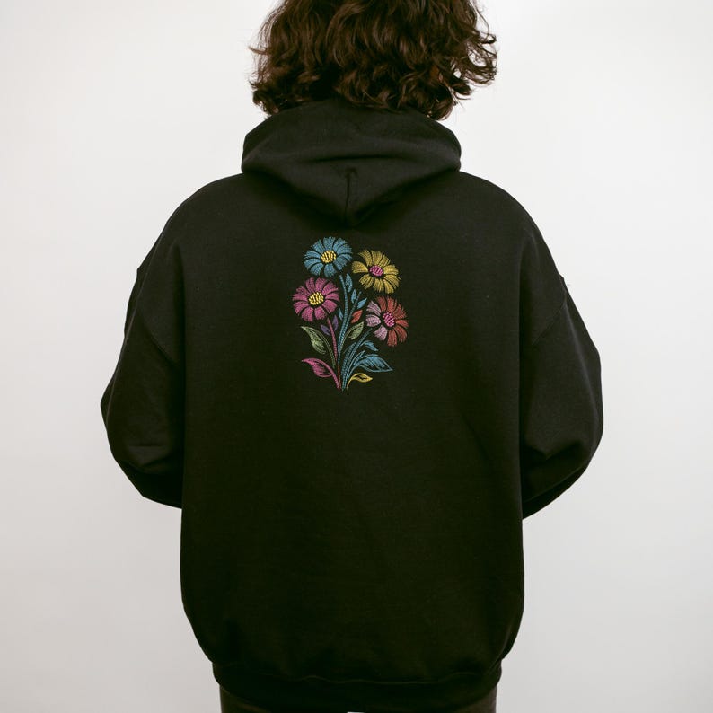 May include: Black hoodie featuring a vibrant floral design on the back. The flowers are in blue, yellow, pink, and purple, with green stems and leaves. The hoodie has a hood and a relaxed fit.