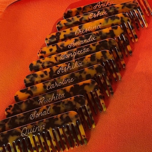 May include: Several tortoiseshell-effect combs, each bearing a different name in cursive lettering. The combs are set at an angle against a bright orange backdrop, creating a striking visual effect.