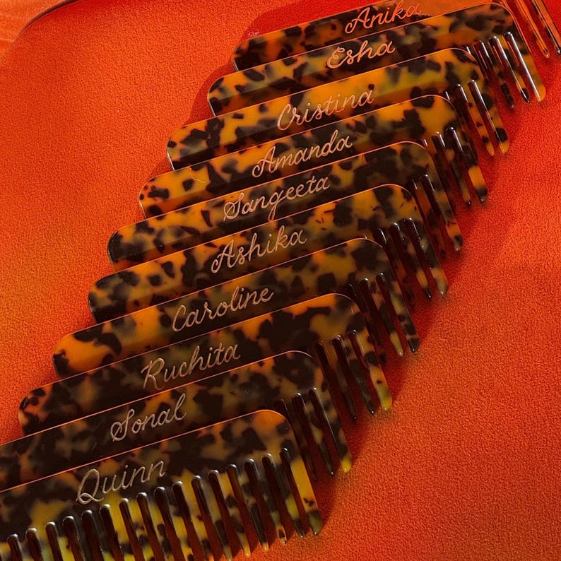 May include: Several tortoiseshell-effect combs, each bearing a different name in cursive lettering. The combs are set at an angle against a bright orange backdrop, creating a striking visual effect.