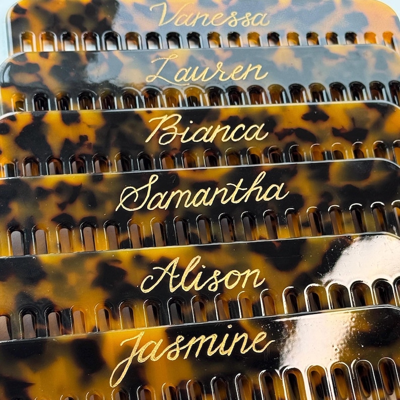 May include: Close-up of several personalized combs with names in gold script. The combs have a tortoiseshell pattern in shades of brown and black. Names include Vanessa, Lauren, Bianca, Samantha, Alison, and Jasmine.