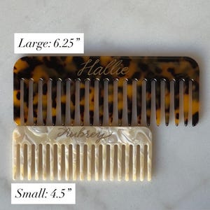 May include: Two personalised combs are shown. The larger comb, 16 cm, has a tortoiseshell pattern and the name "Hallie" in script. The smaller comb, 11.4 cm, is white with the name "Aubrey" in script.